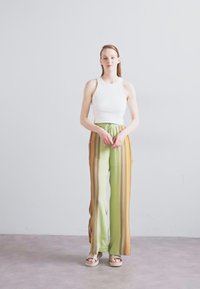 Biely rebrovaný crop top skombinovaný so širokými nohavicami s pruhmi v zelenej a oranžovej farbe, s elastickým pásom a hladkou textúrou. Rybárske sandále dokončujú vzhľad.
