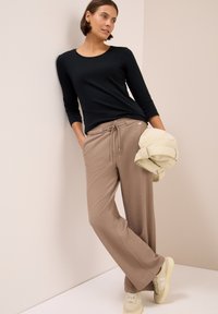 Zwarte lange mouwen top, beige brede broek met trekkoord en lichte sneakers. Zachte textuur met minimale hardwaredetails.