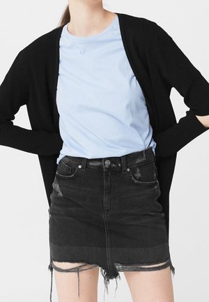 Frau trägt ein hellblaues T-Shirt, eine offene schwarze Strickjacke und einen schwarzen, ausgewaschenen Jeans-Minirock mit ausgefranstem Saum.