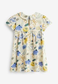 Vestido de niña pequeña de manga corta con cuello redondeado, patrón floral en amarillo, azul, verde y beige sobre un fondo crema.