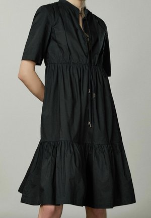 Robe noire à manches courtes avec taille froncée et jupe à volants, dotée d'un détail noué au niveau du col.