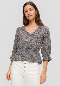 Zwarte en roze bloemetjesblouse met een V-hals, knoopsluiting aan de voorkant en bloemenmouwen, gedragen met witte hoge taillebroeken.
