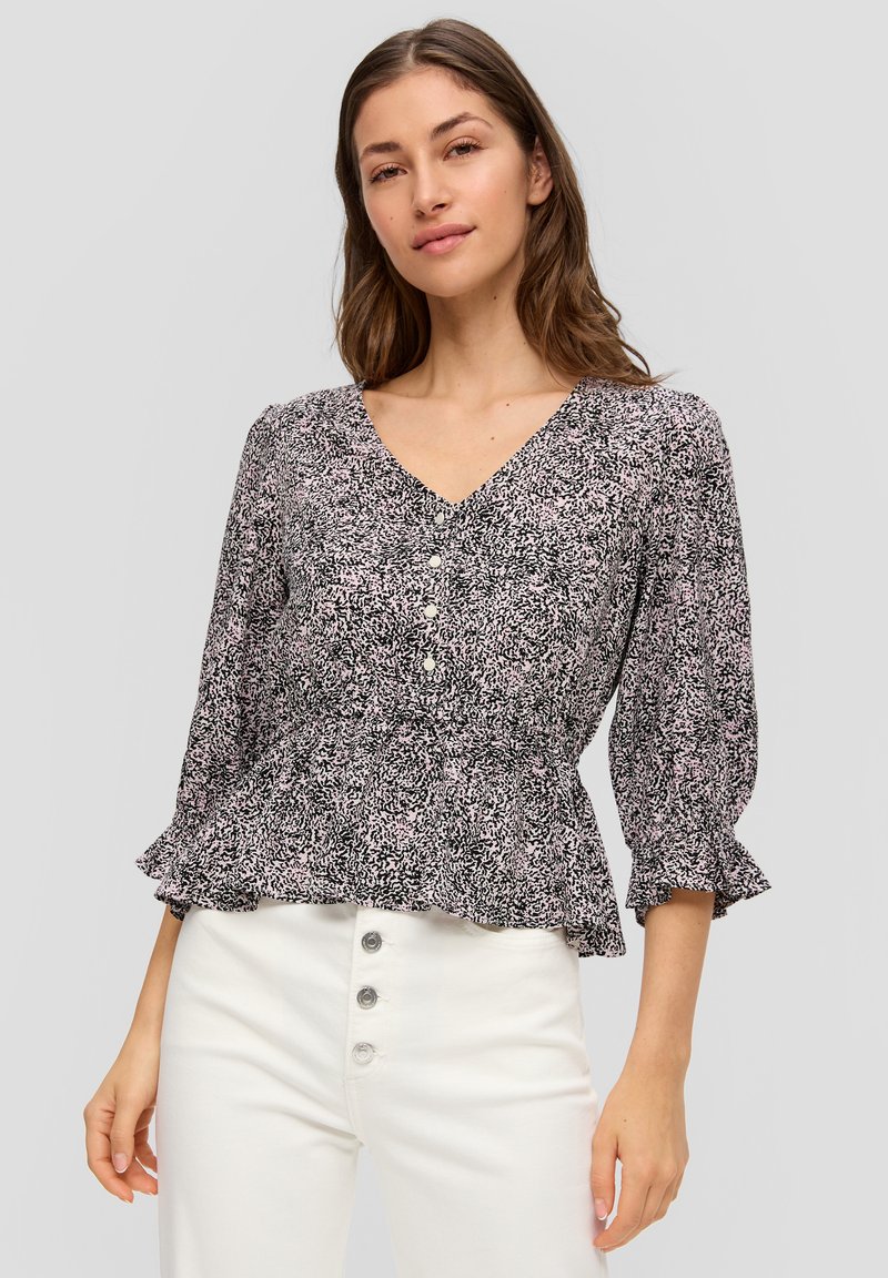 Zwarte en roze bloemetjesblouse met een V-hals, knoopsluiting aan de voorkant en bloemenmouwen, gedragen met witte hoge taillebroeken.
