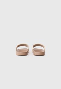 Barna csúszó szandálok, puha, rugalmas talppal. A design minimalista stílusú, nyitott háttal és oldalakkal, sima szintetikus anyagból készült.