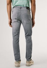 Jeans de denim gris con corte slim, diseño de cinco bolsillos y costuras visibles. Etiqueta de la marca negra en la cintura. Llevados con zapatillas de color claro.