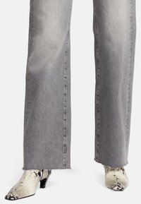 Jeans wide-leg in denim grigio con orlo sfilacciato, abbinati a stivaletti alla caviglia con punta affusolata in stampa serpente bianca e nera a trama.