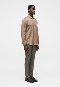 Ανοιχτό καφέ πουκάμισο με κουμπιά και μακριά μανίκια, σε συνδυασμό με υφασμάτινο γκρι παντελόνι και καφέ δερμάτινα παπούτσια. Απλός σχεδιασμός, εφαρμοστή γραμμή.