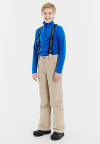 Beige skibroek met bretels, langemmouw blauw shirt en zwarte schoenen. Glad textuur en aansluitend ontwerp voor winteractiviteiten.
