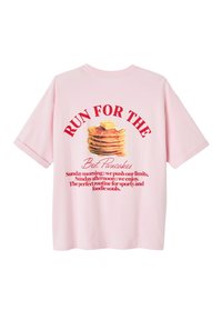 T-shirt en coton rose avec un graphique de crêpes avec du beurre et du texte rouge disant "COURIR POUR LE B… Mais des Crêpes" au dos.