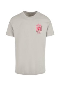 Világosszürke pamut póló kerek nyakkivágással. A bal mellső részen egy piros hímzett Spanyolország címer található. Rövid ujjú.