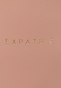 Copertina in ecopelle rosa con testo impresso "EXPATRIÉ" in oro, che presenta una superficie liscia e un design minimalista.