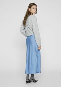 Siva skrajšani pulover v kombinaciji z lahkotno modro satenasto krilo. Outfit ima dolge rokave in gladko teksturo, kar dopolnjujejo črne čevlje in sive nogavice.