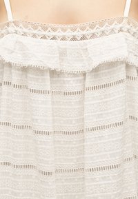 Épaules nues et haut du dos au-dessus d'une robe blanche épaules dénudées avec des motifs floraux en dentelle et brodés.