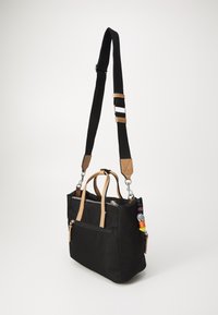 Black nylon handbag with tan leather accents, dual handles, adjustable strap, zippered pocket, and colorful charm attached to zipper.