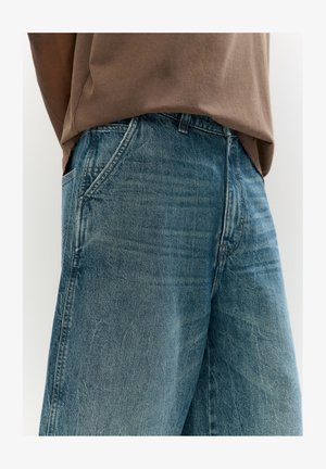Blå denim byxor med vida ben och en urblekt yta, med framfickor och dragkedja. Tyget har en strukturerad, sliten look.