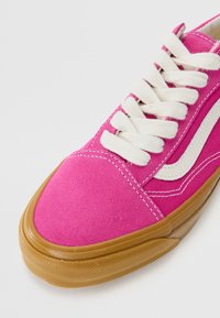 Pink suede sneaker with white laces and side accent. Rounded toe and contrasting gum rubber sole featuring a textured finish.