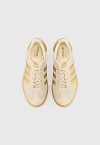Beige athletic shoes with gold stripes, suede and textile materials, round toe, flat rubber sole, and lace-up closure.