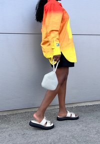 Fel oranje-naar-geel verloop T-shirt, zwarte korte broek, witte en zwarte platformsandalen en een klein wit mesh tasje met een getextureerd oppervlak.