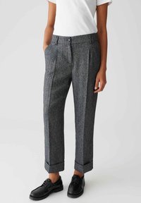 Grau maßgeschneiderte Hose mit einer strukturierten Webart, einfachen Falten, seitlichen Taschen und umgeschlagenen Säumen. Kombiniert mit schwarzen Schuhen.