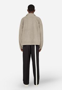 Beige, bolyhos fleece dzseki gallérral, fekete nadrággal, melynek fehér oldalsávja van. Sima tapintású, oversized fazonú.