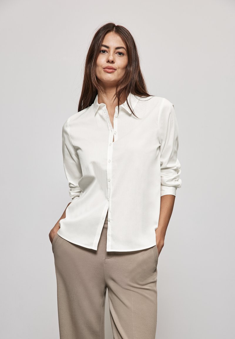 Witte overhemd met een kraag, lange mouwen opgerold, gecombineerd met beige broeken. Glad stof, minimaal ontwerp, subtiele details.