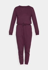 Tuta unica bordeaux con maniche lunghe, collo a giro, vita con coulisse, gambe affusolate e polsini a coste. Tessuto morbido in misto cotone.