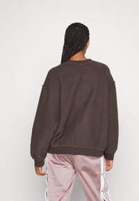 Brązowy polarowy sweatshirt o luźnym kroju i ściągaczach przy mankietach. Tył ma teksturowaną powierzchnię oraz detal w postaci szwu, połączony z różowymi spodniami dresowymi.