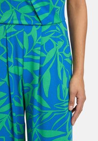 Tissu bleu avec un motif botanique vert, comportant des plis et une taille cintrée. Texture lisse, convenant pour une tenue décontractée ou formelle.