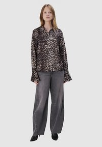 Leoprint Hemd mit Knopfleiste in verschiedenen Braun- und Schwarztönen, langärmlig mit ausgestellten Manschetten, kombiniert mit grauen Jeans mit weitem Bein.