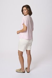 Light pink short-sleeve top paired with white shorts. Model wears beige slip-on shoes. Simple design with a relaxed fit and soft texture.