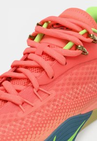 Baskets corail vif avec lacets épais, œillets vert néon et dessus en tissu texturé avec un détail de semelle bleu et vert.