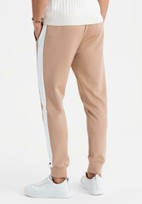 Beiga sportiga joggers med vita sidostråk, tillverkade av ett mjukt material, med en elastisk midja och mudd. Kombinerade med vita sneakers.