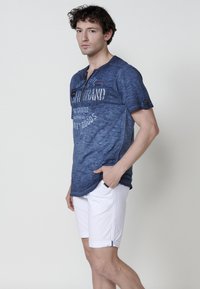 Sininen, lyhythihainen paita henley-kaula-aukolla ja painokuvalla. Yhdistetty valkoisiin shortseihin, joissa on käänteet ja tasku.