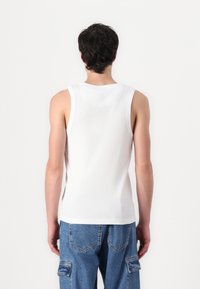 Wit geribbelde tanktop met een ronde halslijn, brede schouderbanden en een aansluitend ontwerp, gecombineerd met lichtblauwe baggy denim broek.