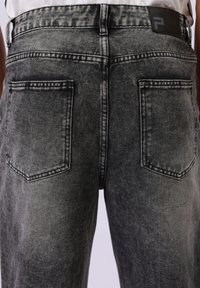 Svarte denimjeans med en falmet vask, som har to baklommer, kontrasterende sømmer og en flat svart etikett på livet.