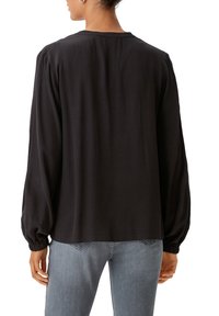 Schwarze Langarmbluse mit lockerer Passform, runder Ausschnitt und elastischen Bündchen. Hergestellt aus weichem Stoff ohne sichtbare Muster.