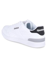 Zapatillas deportivas blancas con parte superior de cuero liso, con un acento gris en el talón y un logo negro en la parte trasera. Suela plana de goma.