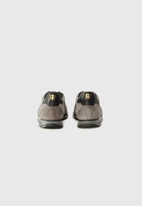 Graue Wildlederschuhe mit einer Ferse aus schwarzem Leder, die ein goldenes Logo trägt. Leichte Gummisohle mit strukturierten Details.
