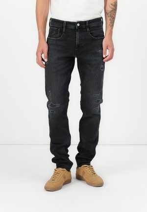 Jeanși negri din denim cu o croială slim, având detalii uzate și un design clasic cu cinci buzunare. Purtați cu adidași bej și o cămașă albă.