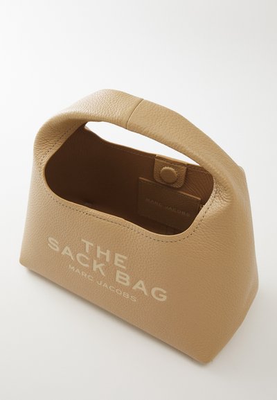 Petit sac à main en cuir beige avec une poignée robuste, ouverture sur le dessus, et "THE SACK BAG MARC JACOBS" imprimé à l'avant.