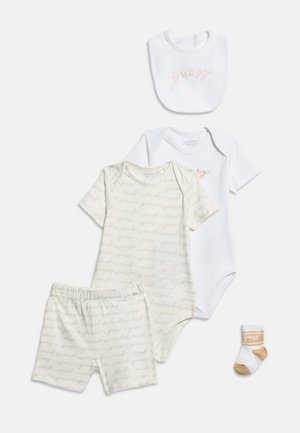 Conjunto de ropa para bebé en blanco y beige que incluye un babero, dos bodies, pantalones cortos con patrón de letras y un calcetín individual con el logo de la marca.