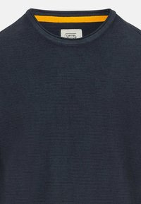 Pull à col rond en maille bleu marine avec un détail orange à l'intérieur du col. Il présente un tissu texturé et une étiquette au niveau du cou.