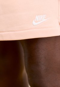 Persikų spalvos Nike šortai, pagaminti iš medvilnės mišinio, su baltu siuvinėjimu logotipo. Lygus paviršius, prigludusi išvaizda, su apatine dalimi virš kelio.