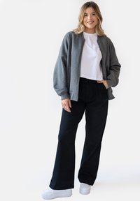 Szara bomberka z zamkiem z przodu, biała krótka koszulka, czarne spodnie z szerokimi nogawkami oraz białe sneakersy na platformach. Gładkie tekstury, swobodny krój.