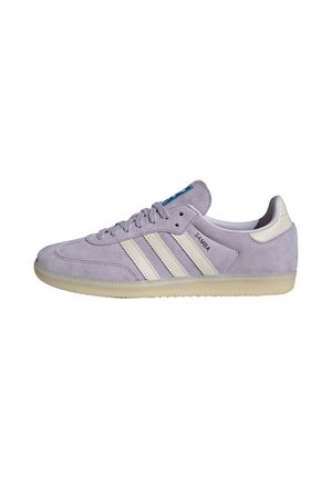 Baskets Adidas Samba en daim violet clair avec des bandes blanches, semelle en gomme et étiquette bleue sur la languette, vue latérale sur fond blanc.
