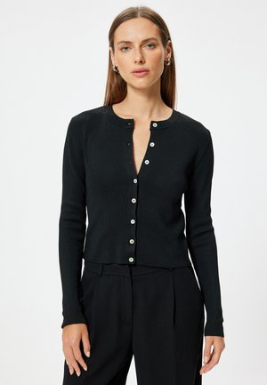 Zwarte geribbelde cardigan met een ronde halslijn, knoopsluiting aan de voorkant en lange mouwen. Kenmerken zijn witte knopen en een cropped ontwerp.