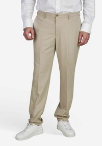 Beige op maat gemaakte broek met een gladde textuur, voorzien van een knoopsluiting en een klassiek platte voorkant ontwerp, gecombineerd met witte sneakers.