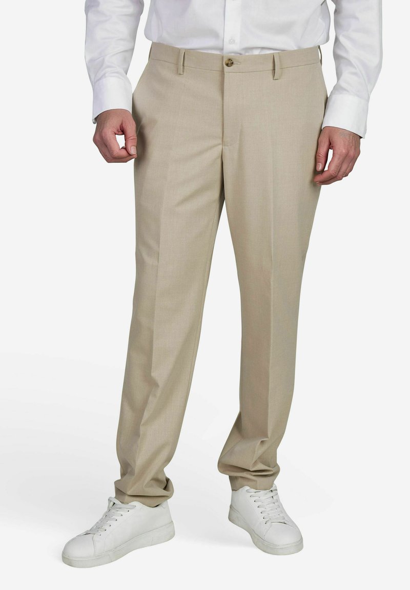 Beige op maat gemaakte broek met een gladde textuur, voorzien van een knoopsluiting en een klassiek platte voorkant ontwerp, gecombineerd met witte sneakers.