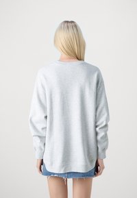 Sudadera gris de manga larga, hecha de tela suave, con un cuello redondo y un corte casual. Usada sobre una falda de mezclilla azul.