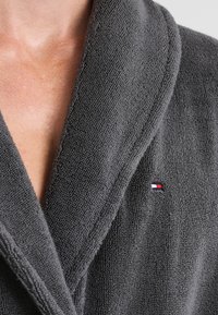 Grau farbener Bademantel aus strukturiertem Stoff, mit Schalkragen und kleinem Tommy Hilfiger-Logo in Rot, Weiß und Blau auf der linken Seite.